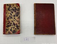 Two antique books with leather covers, one patterned brown and red half-bound and the other reddish-brown full leather with spine wear.