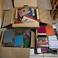 Three large boxes filled with a mixed variety of books showing top views of the contents and visible titles.