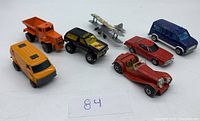 Photo showing all 7 toy cars and 1 toy biplane from front angle on white background.