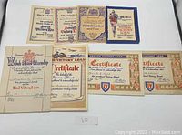 Top-down view of all eight WWII Canadian Victory Loan and Bond certificates arranged on a white surface showing various sizes and printed designs.