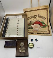 Lot contents showing button sample book in box, wooden carved plaque, Hickory Farms paper bag, Barbie cup, blue rectangular pins, and decorative clock.