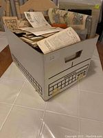 Banker's box filled with assorted vintage paper ephemera and advertisements.