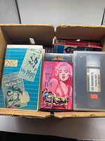 Box containing older VHS tapes viewed from the top showing visible titles and tape cases.