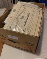 Bankers box containing multiple plastic-sleeved documents with visible certificate on top