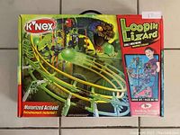 Front of box showing assembled motorized ball machine with loops and a lizard figure graphic, highlighting motorized action and number of pieces included.