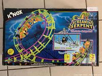 Front of box showing completed roller coaster model with serpent-themed track and loop, riders in coaster cars, brand and product name visible