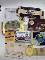 Photo showing an assortment of vintage cigarette and tobacco packaging including Herbert Tareyton, Ogden's, Old Port, Fatima, and Guinea Gold.