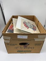 Full cardboard box containing various vintage paper items and ephemera, visible from top with some pieces partially sticking out.