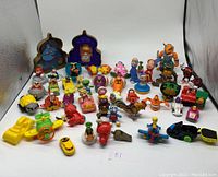 Wide view of various McDonald's and other fast food themed toys including character figurines, vehicles, and playsets arranged on white surface