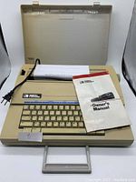 Smith Corona electric typewriter with owner's manual placed on top and a test page loaded, power cord visible, set inside protective case.