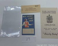 Photo showing the plastic protector sleeve, War Savings Stamp Book with blue cover, and the War Savings Certificates pamphlet side by side.