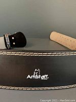 Close-up of Amstaff logo on black leather belt with white stitching.