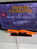 Photo of the arcade game screen with shotgun calibration instruction and the orange light gun controller below the screen.