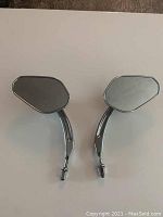 Pair of angular chrome motorcycle mirrors side by side on white background showing front reflective surfaces and chrome stems with threaded mounts.