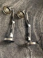 Two chrome industrial style adjustable desk lamps laid on a carpet showing articulated arms and weighted bases.
