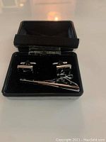 Pair of square silver tone cuff links with black enamel design and a matching tie clip inside a black presentation box.