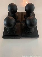 Four black iron deck post tops with round ball finials and square bases, arranged closely together on a surface.