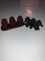 Photo showing both red and dark colored No Evil Monkey figurine sets together on a surface.