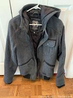 Front view of gray Jack Jones men's medium core workwear jacket with hood, showing zipper closure, chest snap-button pocket, and lower pockets.