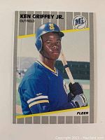 Front side of 1989 Fleer Ken Griffey Jr. rookie card showing player in Seattle Mariners uniform with bat and striped background.