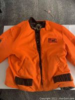 Review of front orange side of the reversible coat with visible pockets and brown knit cuffs.