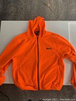 Front view of bright orange fleece hoodie with hood and full zipper laid flat on surface.