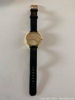 Full view of the Nixon women's wristwatch showing the black leather band and gold-tone round dial face.