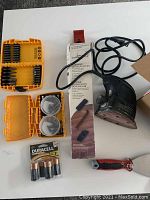 Electric detail sander, screwdriver bits sets, putty knife, and Duracell batteries arranged on a white surface.