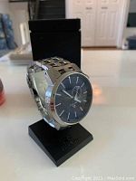 Silver-tone stainless steel Rip Curl wristwatch with linked bracelet and black dial on black display mount.