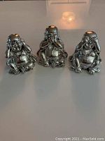 Photo of the three shiny Buddha statues together on a flat surface showing the full set.