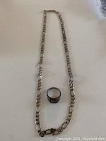 Sterling silver chain necklace with broken clasp, laid out flat with silver ring in center.