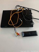 Top view of black Sony DVD player with attached cables and a remote control displayed in front