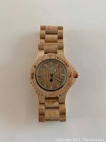 Front view of wooden wristwatch showing wood grain dial with white hands, markings, and wooden bezel with brand engraving.