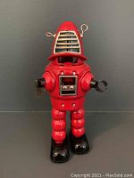 Front view of the red wind-up robot toy showing the details on the head, arms, and torso, with visible broken claw hand.