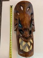 Front view of the wooden carved mask with tape measure showing height approx 22 inches.