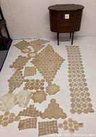 Full view of the antique sewing table with numerous crocheted doilies laid out on the floor in front.