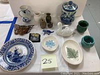 Full display of assorted art pottery pieces, plates, figurines, and small vases on white and blue cloth.