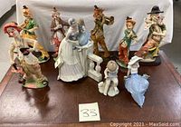 Nine collectible figurines arranged on a wooden surface including clowns, musicians, and a woman with child.