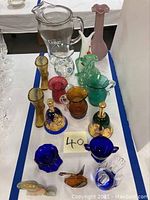 Full lot arranged on table showing various colored glass decorative items including pitchers, vases, and figurines.