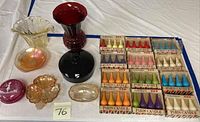 Two colored glass vases, decorative dishes, and 15 boxes of vintage Paris Candles arranged on a table