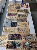 Wide shot of table with multiple wooden trays filled with assorted costume jewelry including necklaces, bracelets, rings, and brooches excluding wooden trays from the sale