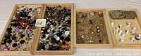Two wooden trays filled with a large assortment of buttons in varied colors, sizes, and styles, alongside a wooden tray with assorted jewelry pieces and ceramic thimbles.