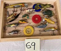 Image of assorted fishing lures and accessories inside a wooden tray, showing various shapes, colors, and hooks.