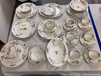Full set of Haviland Limoges china including cups, saucers, plates, bowls, creamer, and platter arranged on white cloth surface.