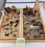 Overview of lot showing two wooden trays full of assorted small collectible animal and character figurines in various colors and sizes.