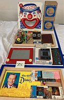 Lot overview showing carnival clown sandbag toss game face, boxed electronic game PacMan2, Disney ephemera, Magna Doodle board, and assorted game items on wooden tray (tray not included).