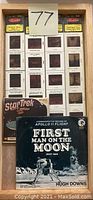 View of wooden tray holding Apollo 11 LP, Star Trek picture slides, and stereo photos with a lot number card visible