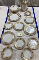 Wide view of the Noritake china set including various plates, bowls, covered casserole, and coffee pot, all resting on a white cloth.