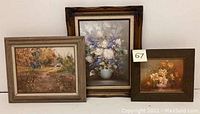 Wide shot of the three paintings with floral and countryside themes, showing frames and overall condition.