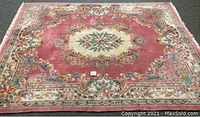 Full view of the oriental area rug showing the medallion and surrounding floral designs on a pink field with a cream border.